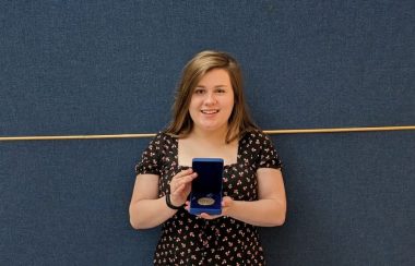 Emily Plamondon sourit à la caméra avec sa médaille de la gouverneure générale en main.