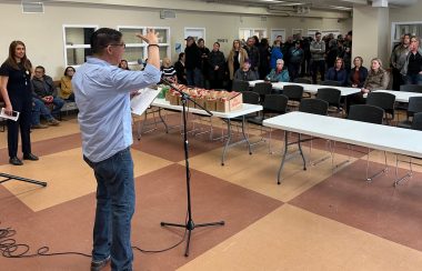 A speaker stands in front of a group of people, with a few fold-up tables in front of him. The photo is taken inside of the Lethbridge Wellness Centre.