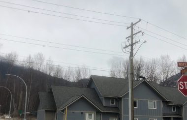 Stop and street signs in the foreground, top of a housing development in the background.