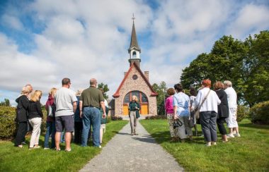 Des gens debout en face dune petite église en roches par une journée d'été.