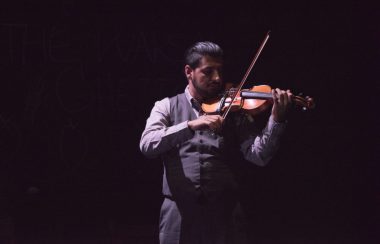 Sari Alesh standing on a stage and playing violin in front of a black backdrop.