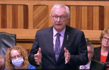Le premier ministre du Nouveau-Brunswick, Blaine Higgs, à l'assemblée législative, vêtu d'un habit noir et d'une cravate bleu devant des membres de son parti politique