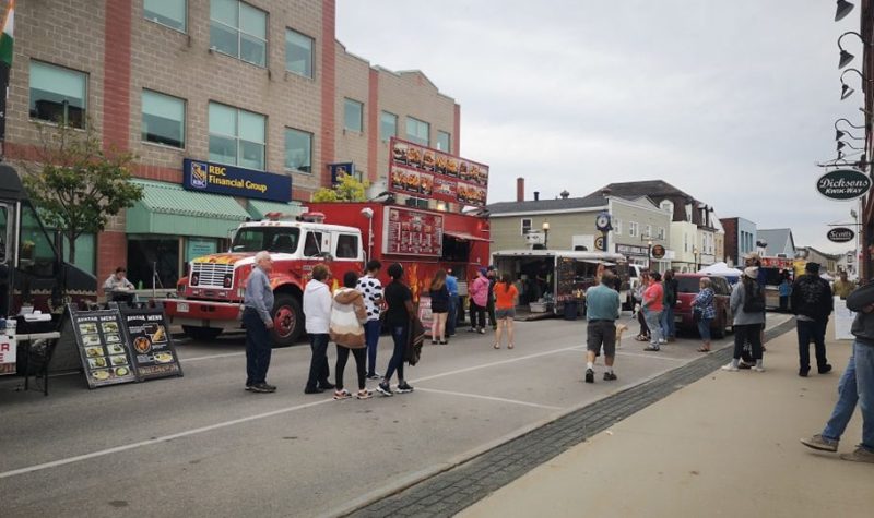 Plan large sur les festivités, avec une rue piétonnière et des camions de nourriture de rue.