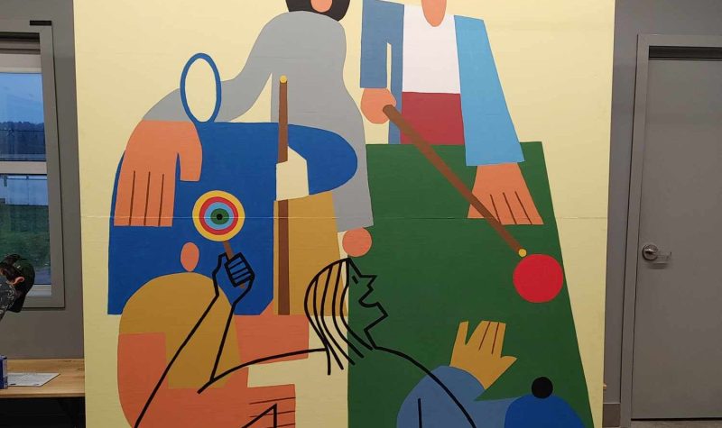 Pictured is the urban mural completed by Sutton. It depicts youth from the Maison des jeunes playing some of their favourite activities and spending time with friends. The mural is made up of simple geometric shapes and its primary colours are blue green, and orange. The background of the mural is painted yellow.