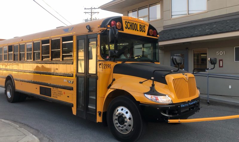 A yellow school bus sits outside of a beige building,