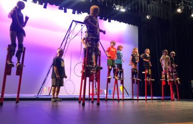 Children on a stage on stilts in purple light.