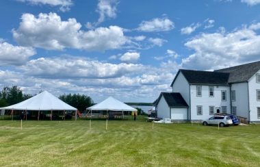 Plan large sur le site de la Mission de Lac La Biche où se dérouleront les festivités, avec deux grandes tentes et une bâtisse à gauche.