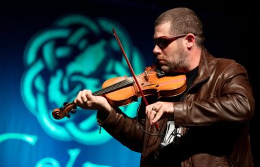 Un violoneux portant un gilet brun et des lunettes à soleil.