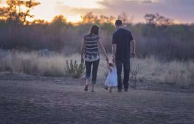 A couple walking towards forest at sunset holding a child's hands