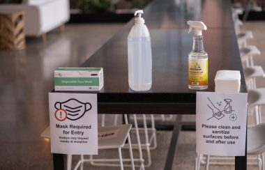 A picture of a black table with hand sanitizer on it and signs about COVID-19 hygiene.