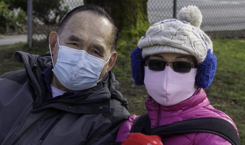 Two people wear masks and winter gear outside in Vancouver