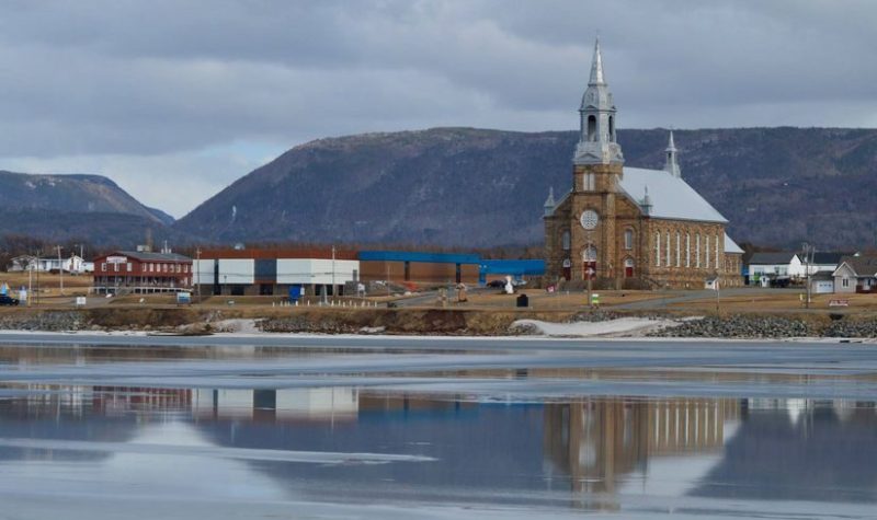 Église et école situées en avant d'une baie avec les montagnes en arrière plan.