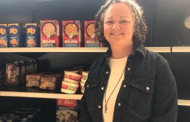 A woman poses in front of non-perishable foods on a shelf.