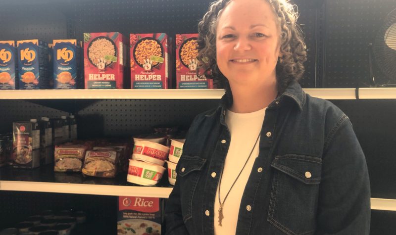 A woman poses in front of non-perishable foods on a shelf.