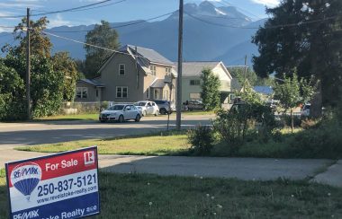 For sale sign in the foreground, houses and mountains in the background.