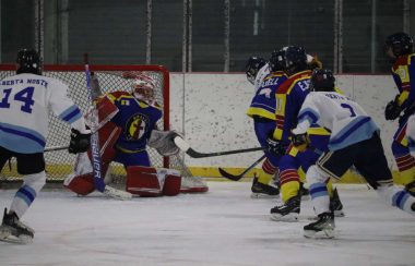 A hockey game going on with players from both side skating towards the net with the puck lying on the goalies left.