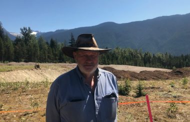 A man with a hat on standing in the sun against a backdrop of mountains.