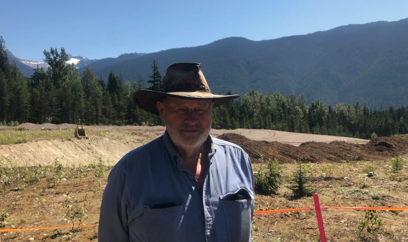 A man with a hat on standing in the sun against a backdrop of mountains.