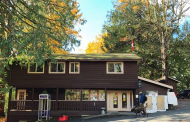 A two-story brown building is set on a gentle slope with a phone booth in front.