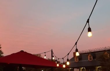 The sun sets and the sky is blue and pink. a string of lights is visible lining the sidewalk. across the street, there is the Kingston Visitor Information Centre
