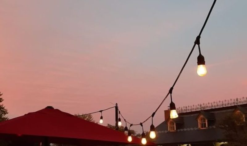 The sun sets and the sky is blue and pink. a string of lights is visible lining the sidewalk. across the street, there is the Kingston Visitor Information Centre