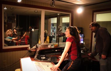 Alyson Roussel, en avant plan, debout, en train d'animer la radio dans les studios éclairés de Boréal FM.