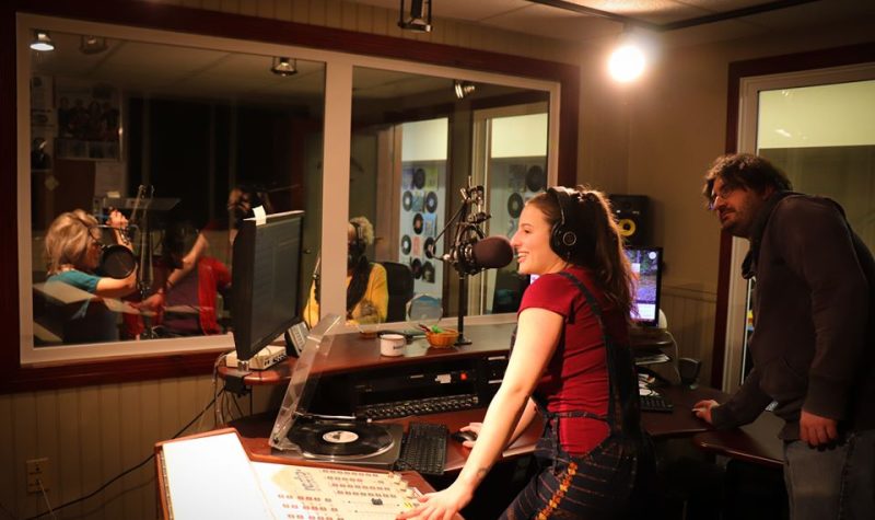 Alyson Roussel, en avant plan, debout, en train d'animer la radio dans les studios éclairés de Boréal FM.