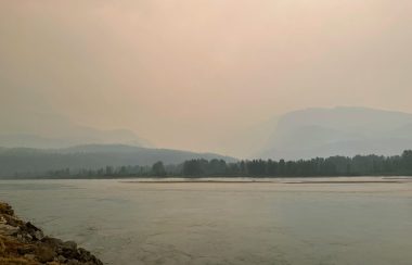 A lake with mountains in the background. The mountains are shrouded in a haze of wildfire smoke.