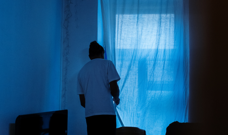 un joven observa temeroso por una ventana. Foto: canva.com