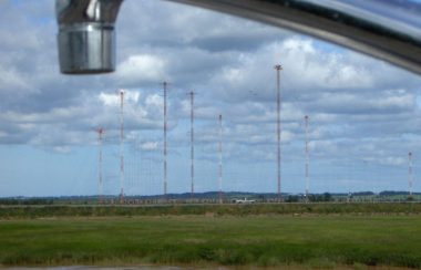 In the foreground, a stainless steel tap in the top of the photo frame, and in the distance, metal radio towers on a green flat landscape.