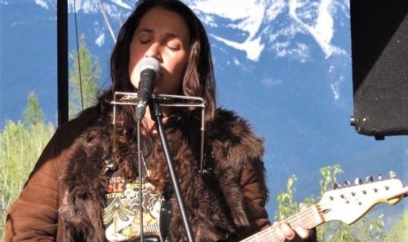 Avery playing guitar and singing. Mountains and trees in the background.