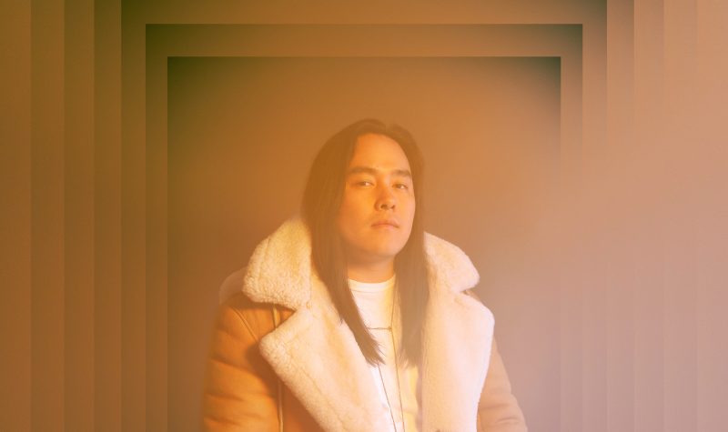 Man with long hair sitting in suede jacket, lookign at camera, orange filter cover the image