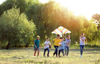 Un groupe de six enfants courent dans un champ avec un cerf-volant multicolore.