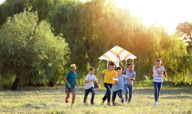 Un groupe de six enfants courent dans un champ avec un cerf-volant multicolore.
