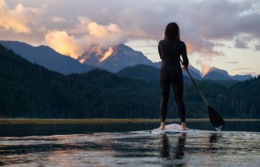 A person a paddle board at sunset with mountains in the background