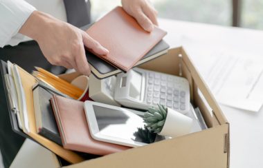 Une personne range des cahiers, une tablette électronique, une calculatrice et une plante dans une boîte.