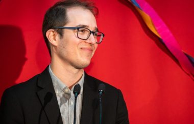 Monsieur Alexandre Leduc vêtu d'une veste noire sur chemise grise, devant un fond rouge