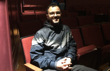 A young man sitting in a movie theatre, smiling.