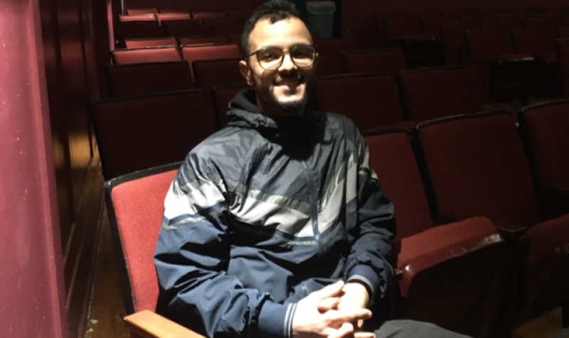 A young man sitting in a movie theatre, smiling.