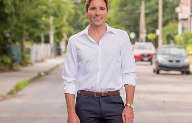 A person in a white dress shirt and grey pants is standing outside on a street.