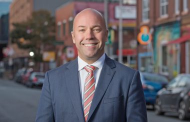 Portrait photo of MP Andy Fillmore. He is smiling in a blue suit, and downtown Halifax is in the background.
