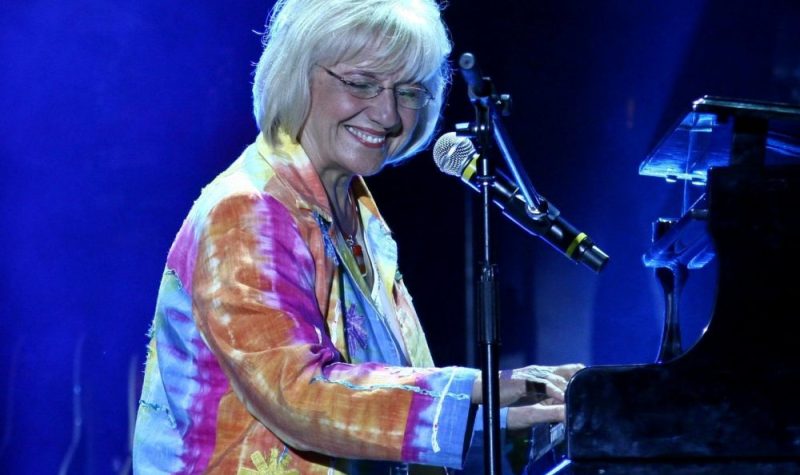 Une femme portant un gilet multicolore qui chante et joue du piano.