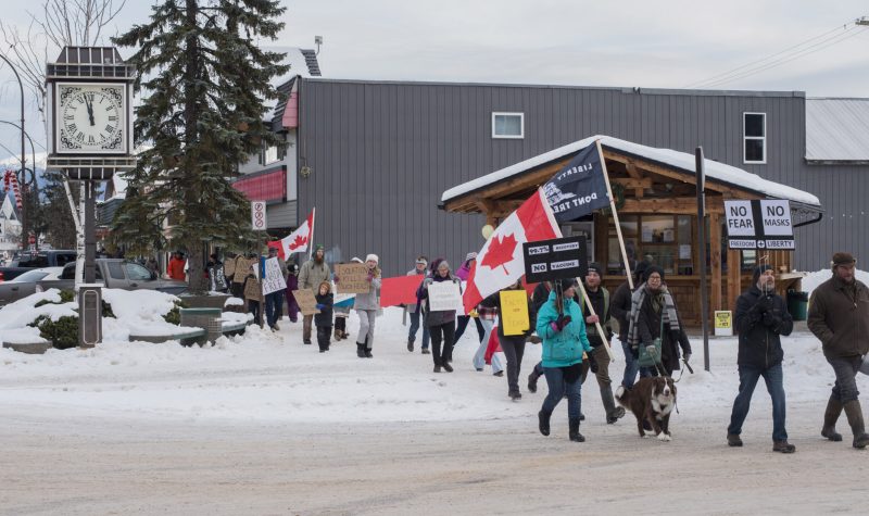 A group of people walk with flags to protest wearing masks in downtown Smithers