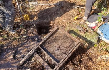 A wooden framed screen lays next to a square hole in the ground