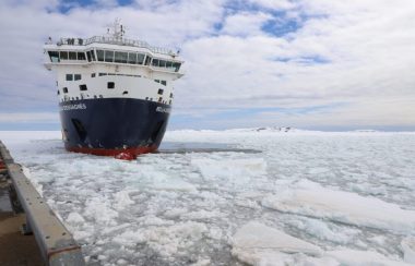 Un navire à l'approche d'un quai qu'on voit à peine est entouré de morceaux de glace sur une vaste étendue d'eau.