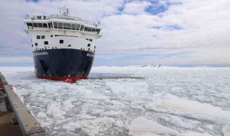 Un navire à l'approche d'un quai qu'on voit à peine est entouré de morceaux de glace sur une vaste étendue d'eau.