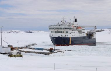 Un navire à l'approche d'un quai entouré de morceaux de glace sur une vaste étendue d'eau.