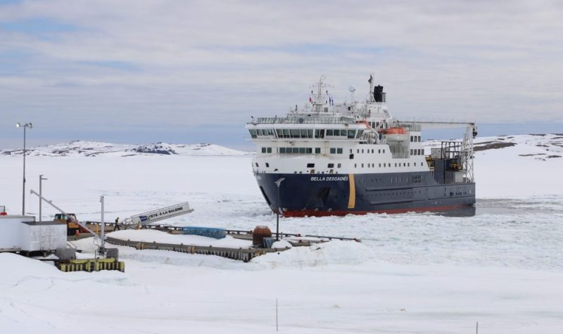 Un navire à l'approche d'un quai entouré de morceaux de glace sur une vaste étendue d'eau.