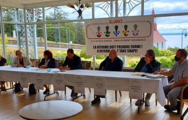 Membres de l'alliance interprovinciale dans une salle vitrée avec temps dégagé et fleuve au loin.