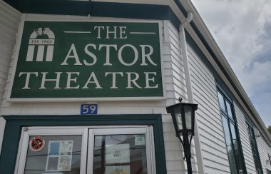 Sign for the Astor Theatre above glass double-doors in a white building